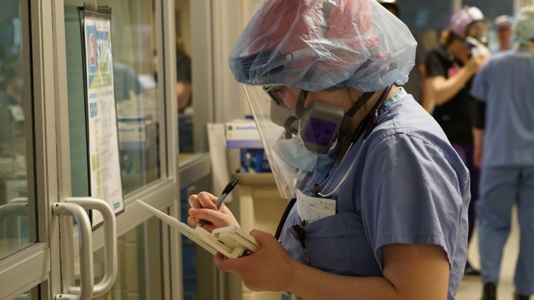 A nurse with personal protective equipment writing on a tablet.