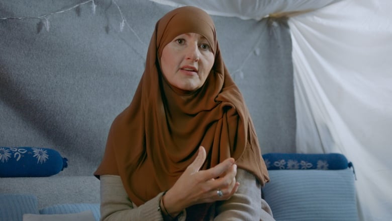 A white woman in a hijab speaks to a camera.