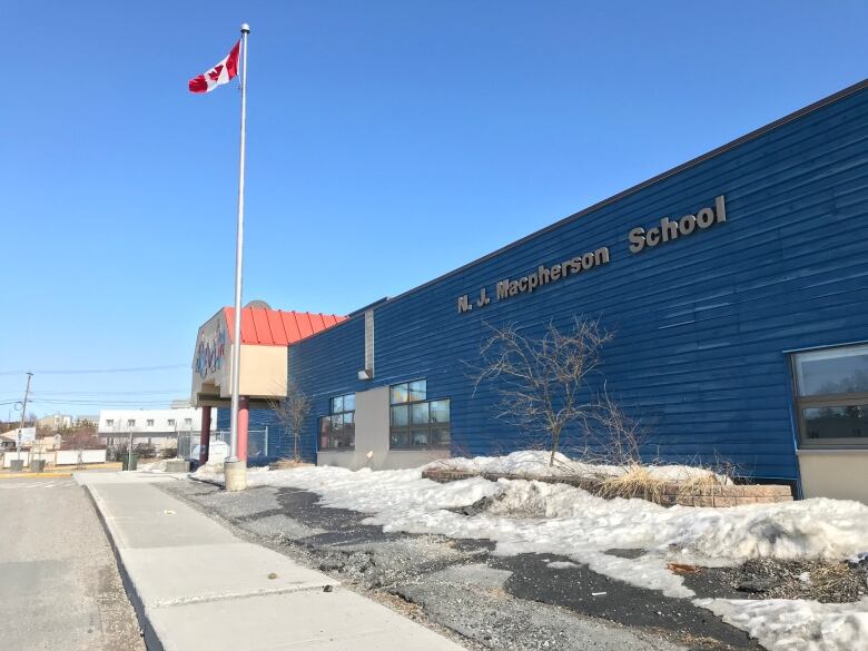 A blue building with a Canadian flag in front stands before a blue sky. 