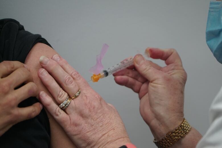 A close-up of a pharmacist's hands injecting a vaccine into a person's arm.