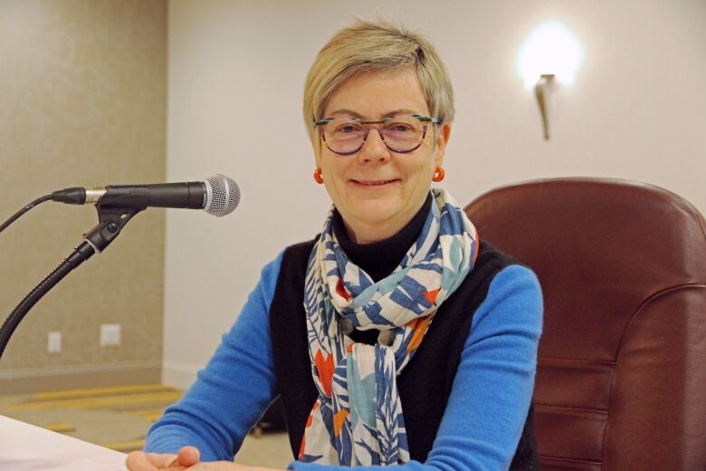 Woman sitting at table with mic in front of her smiling at camera.