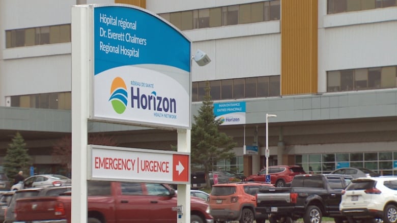 A large sign in front of a large building with a busy parking lot reads, Dr. Everett Chalmers Regional Hospital, emergency.