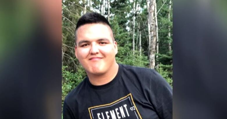 Braden Herman is posing for a photo from the chest up in a black shirt and there is greenery in the background