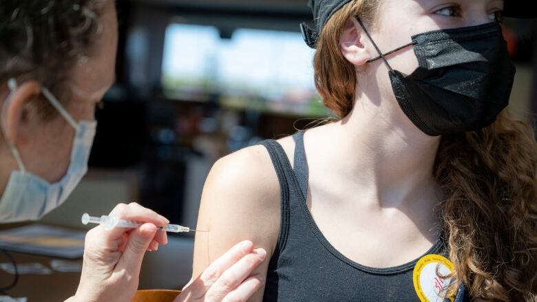 A kid wearing a mask gets vaccinated in the arm.