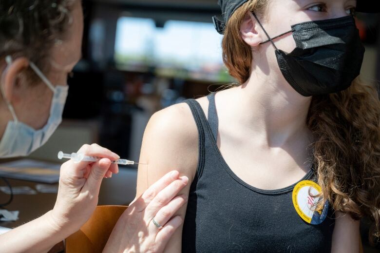 A kid wearing a mask gets vaccinated in the arm.