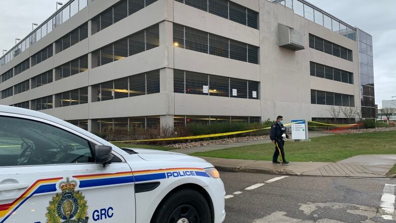 A RCMP car is parked in front of a 5-storey parkade on a summer day. 