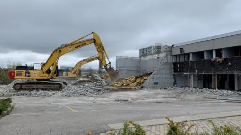 A backhoe breaks concrete off a building.