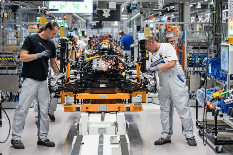 Two men assemble a car engine in a factory.