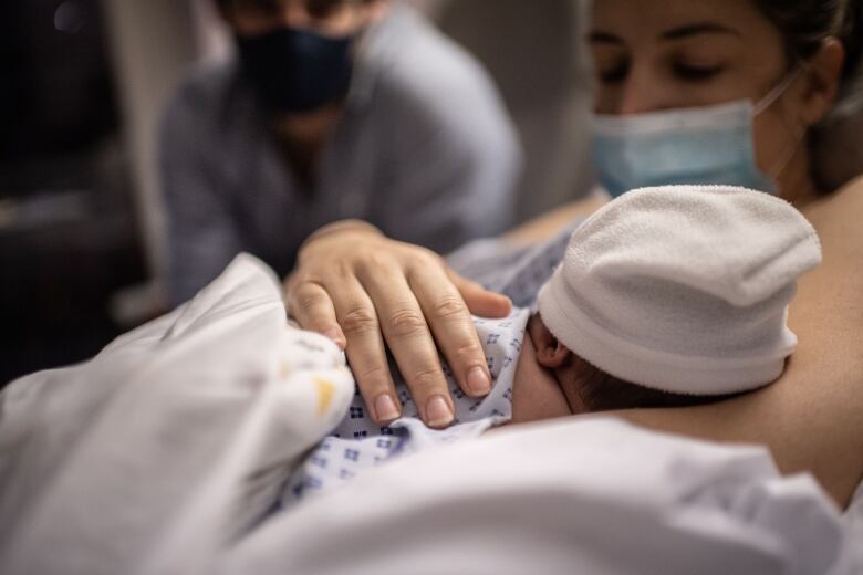 A newborn baby snuggles into their mother in a hospital bed. Their father looks on in the background. 