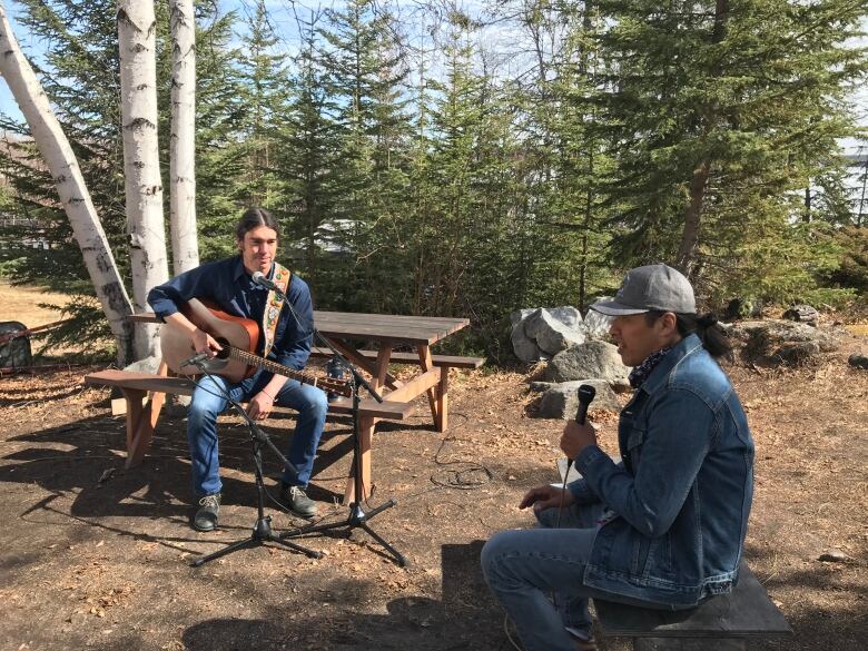 Musician Jay Gilday speaks to Lawrence Nayally outside on the shores of Yellowknife Bay on a bright sunny day.