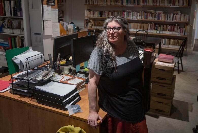 A woman with curly gray-black hair looks away from the camera in a library-style room.