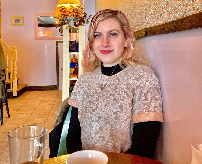 a woman with blonde hair sits in front of a pink wall