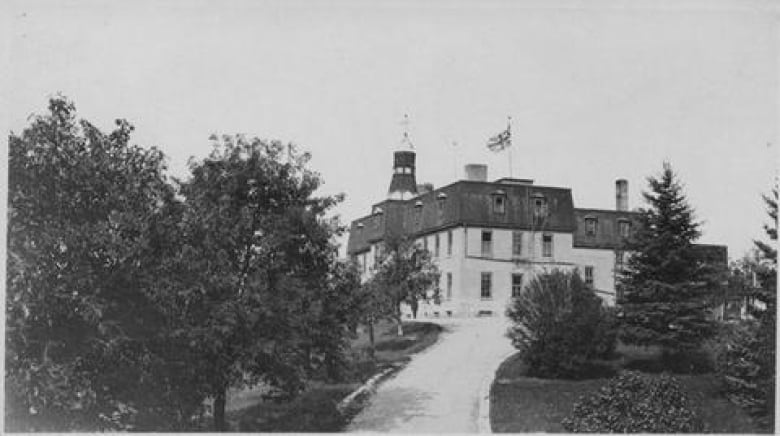 Old picture of a building up a road flanked by trees.