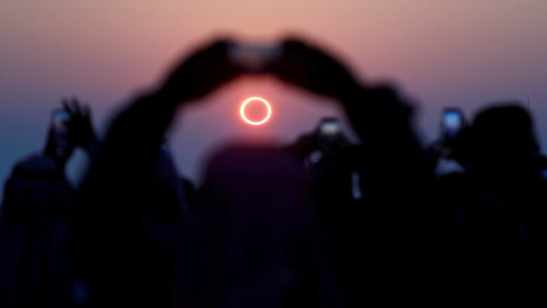 People in a crowd holding cameras and cellphones raise their arms as they take photos during a solar eclipse.