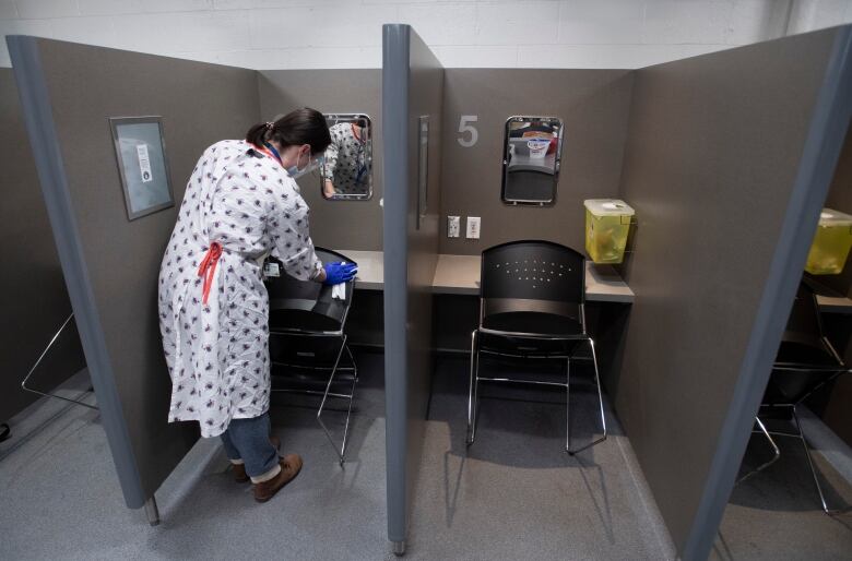 A woman in a white gown cleans the backside of a chair, located in a narrow booth.