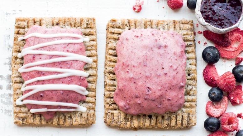 Overhead shot of 2 rectangular pastry tarts on a marble surface. They're topped with pink icing. Strawberries, blueberries and raspberries sit on the left side of the image, along with a small white jar of berry jam. 