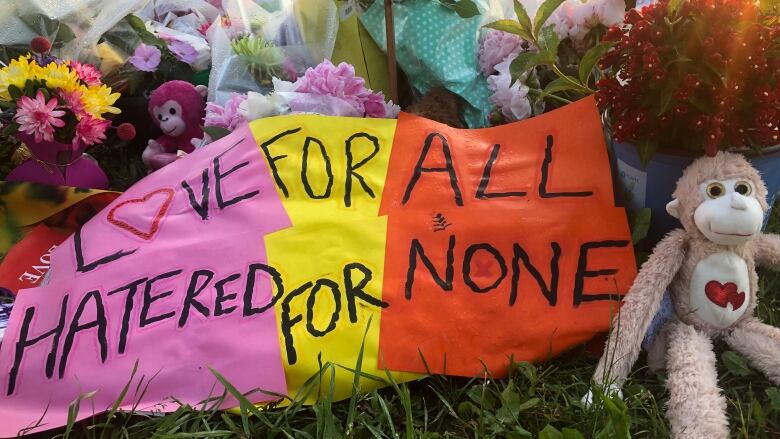 A memorial made up of flowers, a stuffed animal and a banner that says 'Love for all, hatred for none.'