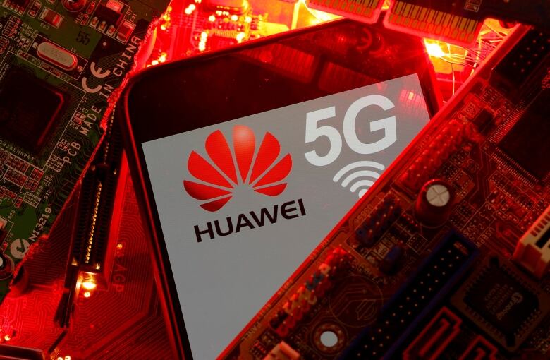 A cellphone with a logo and text reading Huawei 5G sits on a background of computer chips.