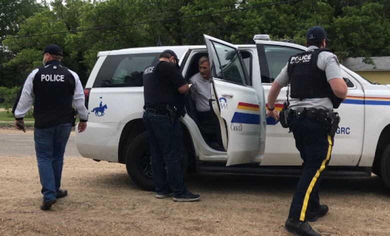 RCMP officers are seen putting a man in the back of an SUV police cruiser