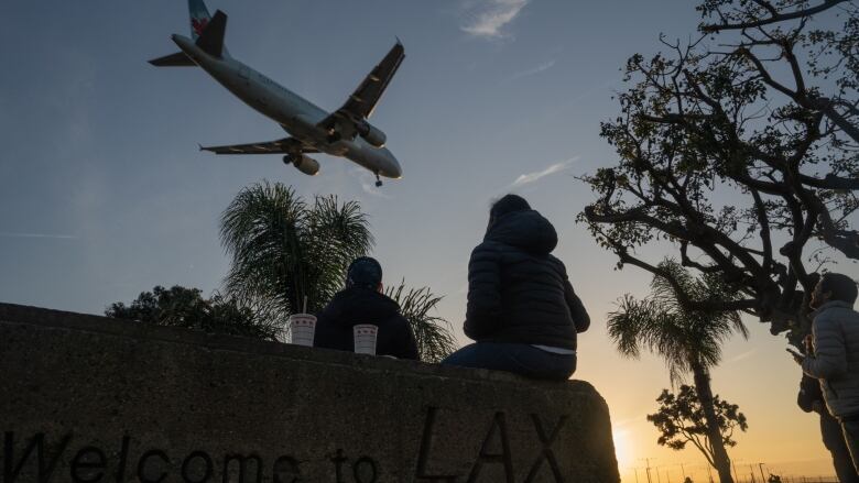 People on the ground watch an Air Canada jet fly over LAX airport.