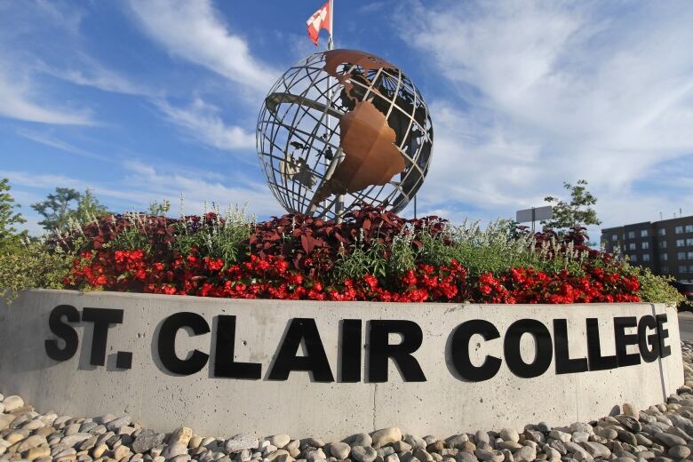 A sculpture of a globe in front of a sign that says St. Clair College.