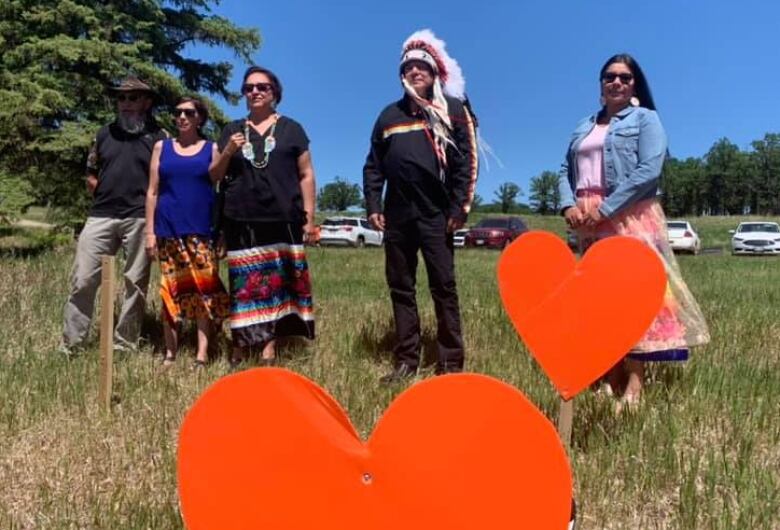 Indigenous leaders stand by large orange heart memorials.