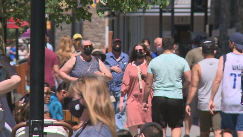 Crowds walk down a busy sidewalk. 