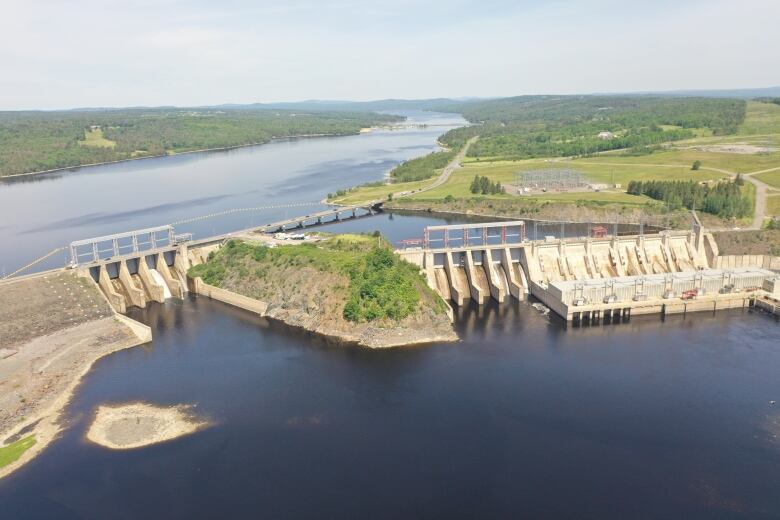 An aerial shot of a dam surrounded by water with green grass and trees on the banks.