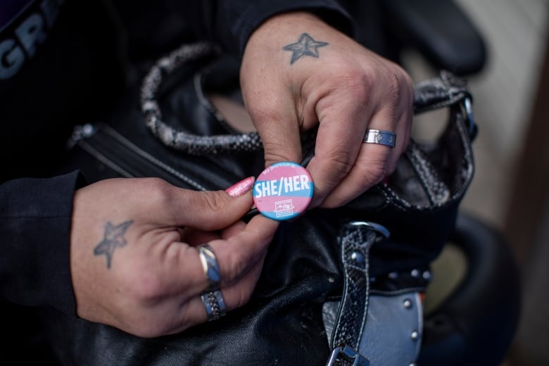 A pair of hands hold a pin in pink, blue and white colours.