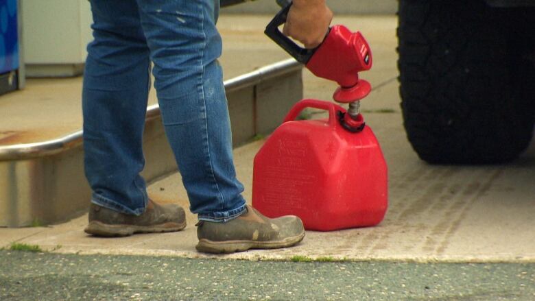 A man pumps gas into a red gas tank.