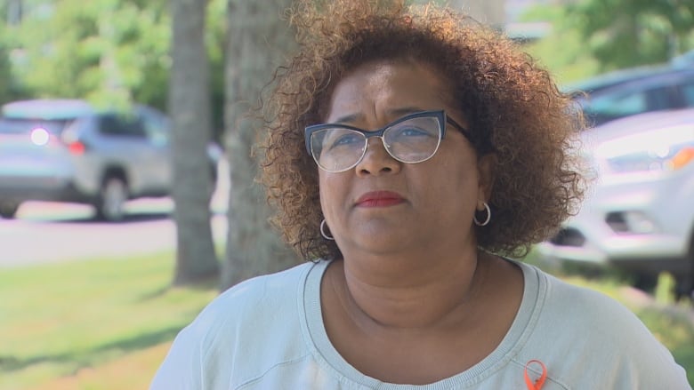 A Black woman with brown, curly hair is wearing glasses and a light green top