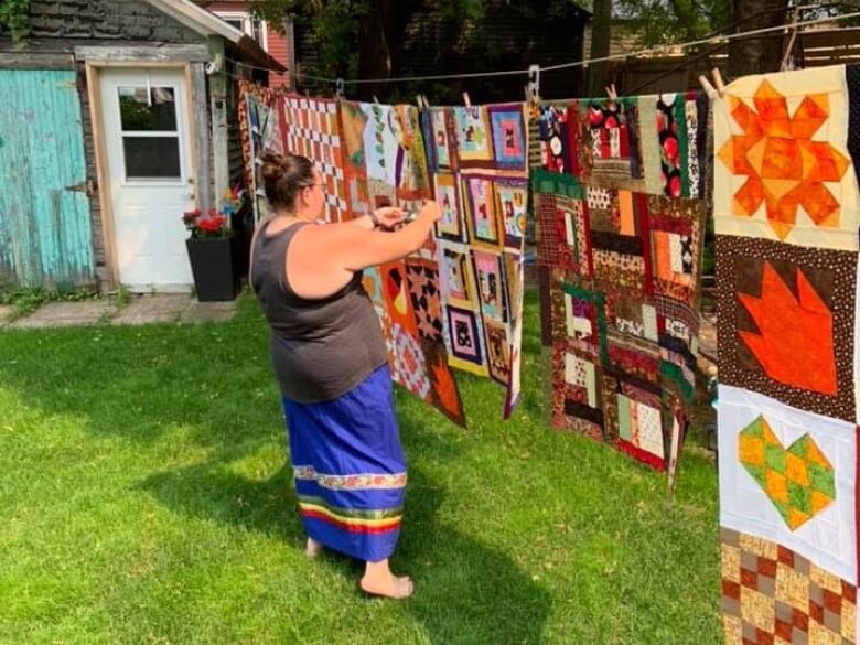 A woman arranging quilts on a clothing line.