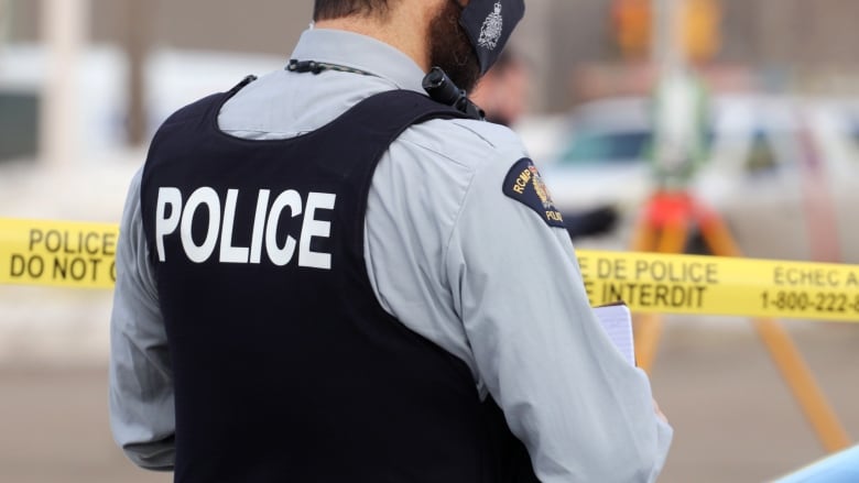 A police officer wears a vest that says police in front of crime scene tape.