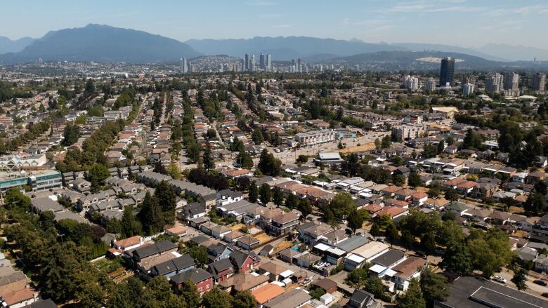 An aerial shot of rows of houses in Vancouver, with high rises and mountains visible in the distance.