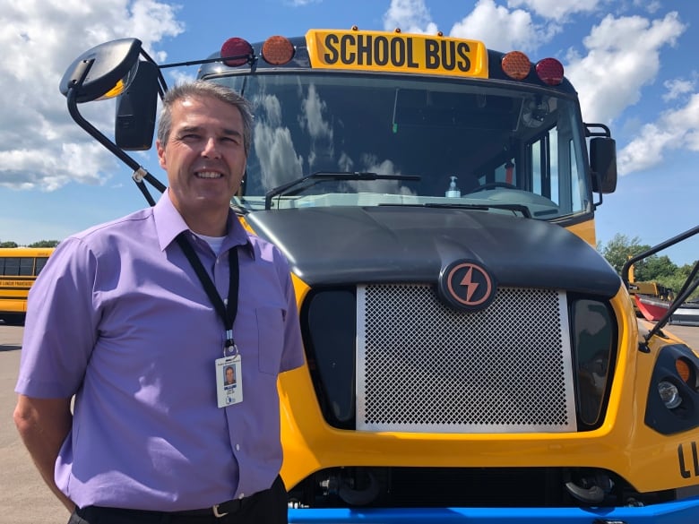 A man stands in front of an electric school bus. 