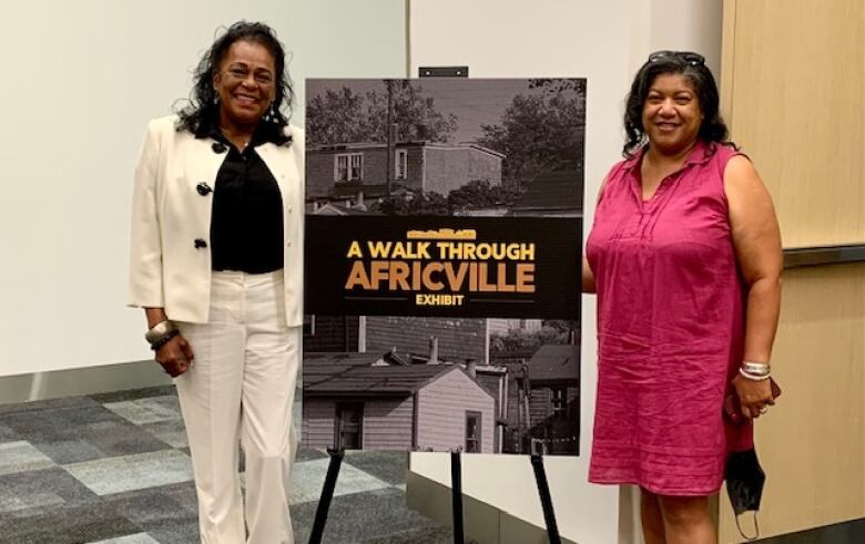 Two Black women stand behind a sign that reads 