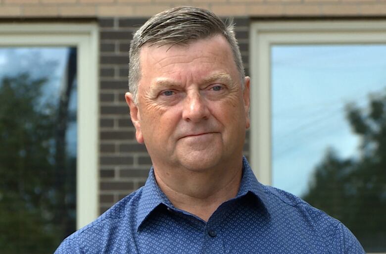 A middle-aged man wearing a blue shirt looks slightly to the right of the camera.