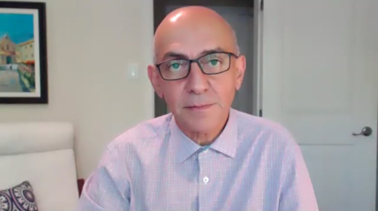 A bald man in rectangular glasses looks into the camera on a video call.