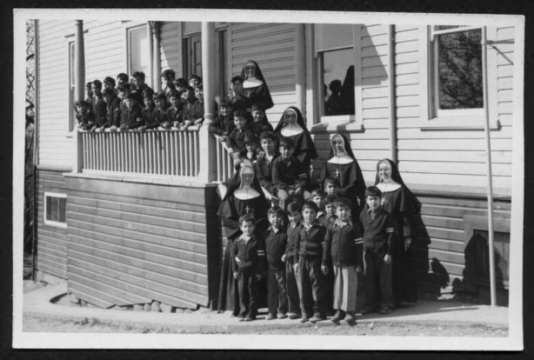 A black-and-white picture of a group of nuns, lined up along with dozens of Indigenous kids.