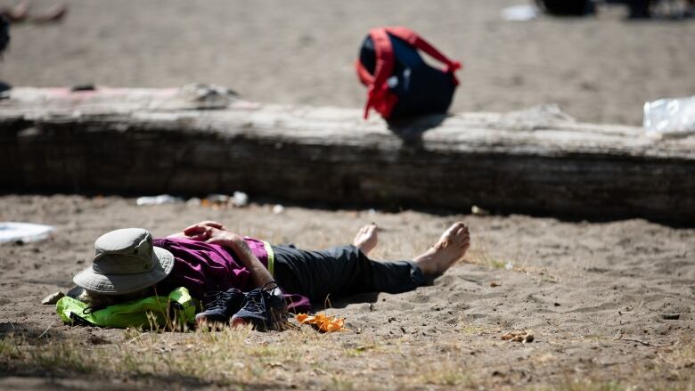 A person lies in the sun with a wide-brimmed hat over their face at Kitsilano Beach in Vancouver on Tuesday, August 10, 2021.