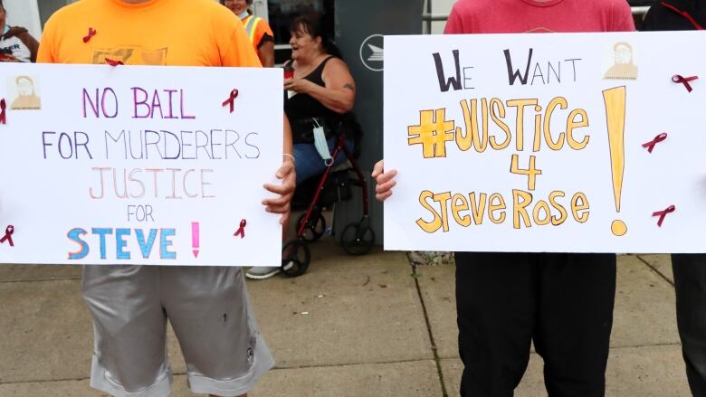 Two protest signs are seen being held. One reading: No Bail for Murders Justice for Steve. The other: We want #Justice for Steve Rose.