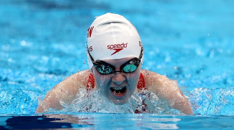 A woman wearing goggles and a swim cap emerges from the water mid-stroke