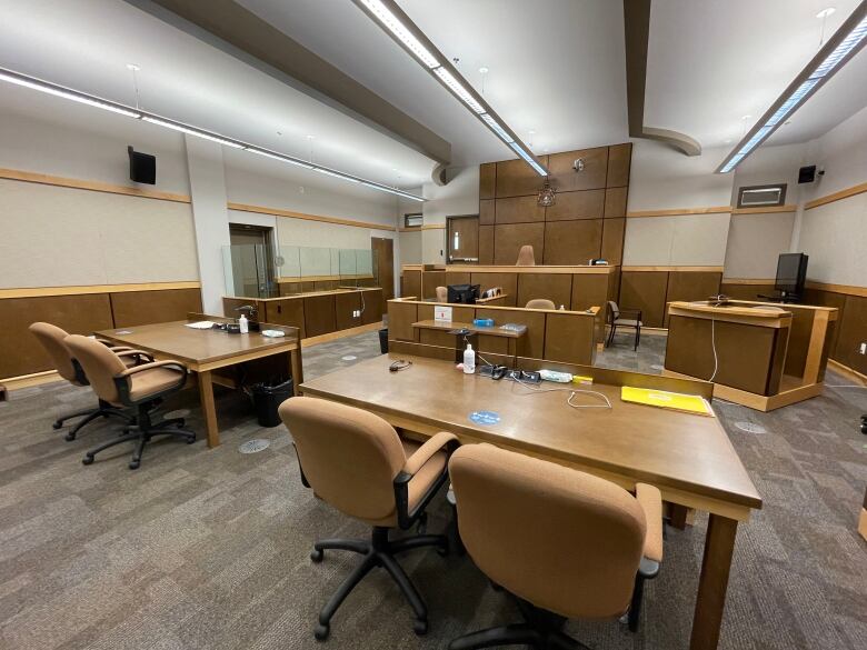 A courtroom with two tables with chairs in the foreground, a dais in the background where the judge sits, a witness stand to the right and a prisoner's box on the left.