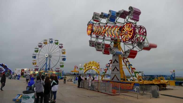 Fair rides, including a ferris wheel, are pictured outside under a dark and cloudy sky.