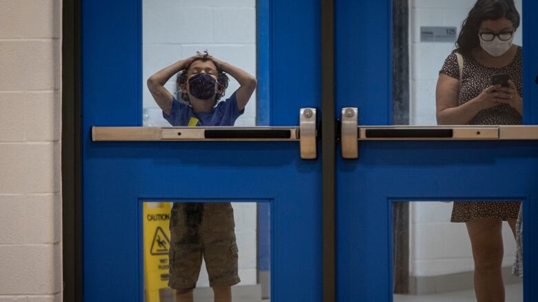 A child in a doorway with their hands on their head.