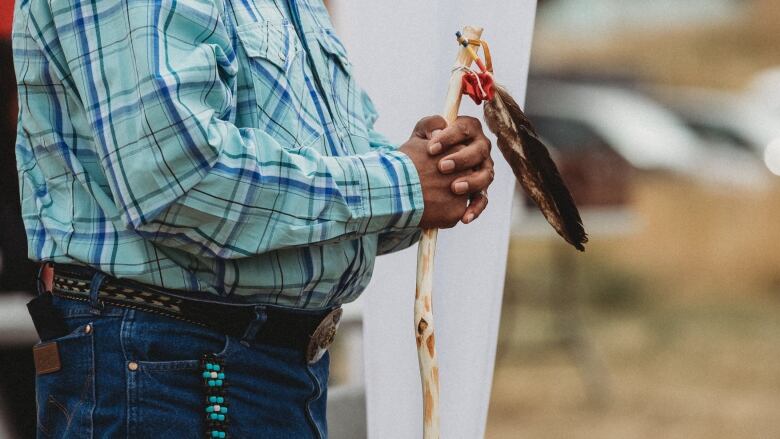 A man holds a staff with a feather atop it.