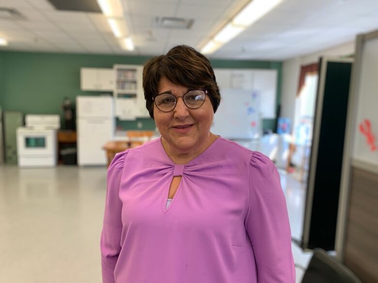 A woman in a fuchsia blouse and wearing glasses looks at the camera.