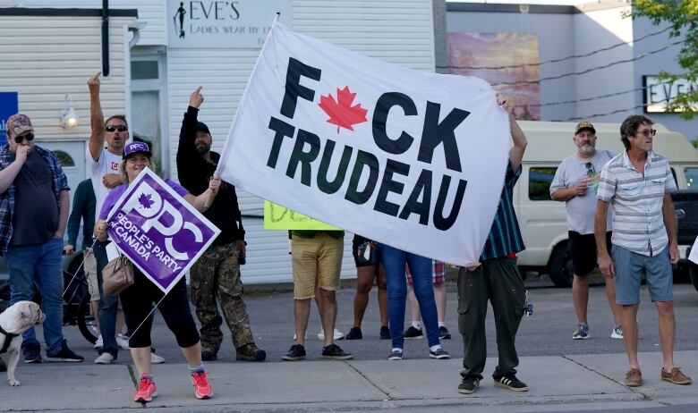 At a small protest, two people hold a flag with a vulgar message about the prime minister.