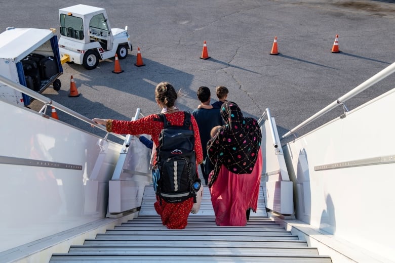 Two women and two men dressed in traditional clothes descend an airport staircase onto the airport tarmac.