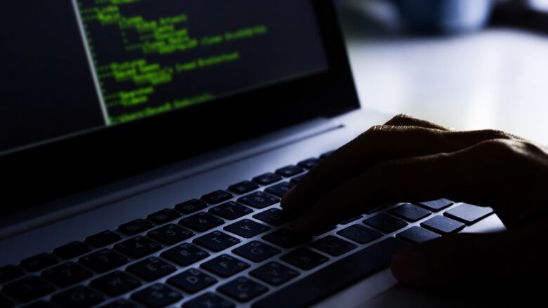 A closeup shows a hand typing on a computer keyboard in a dimly lit room.